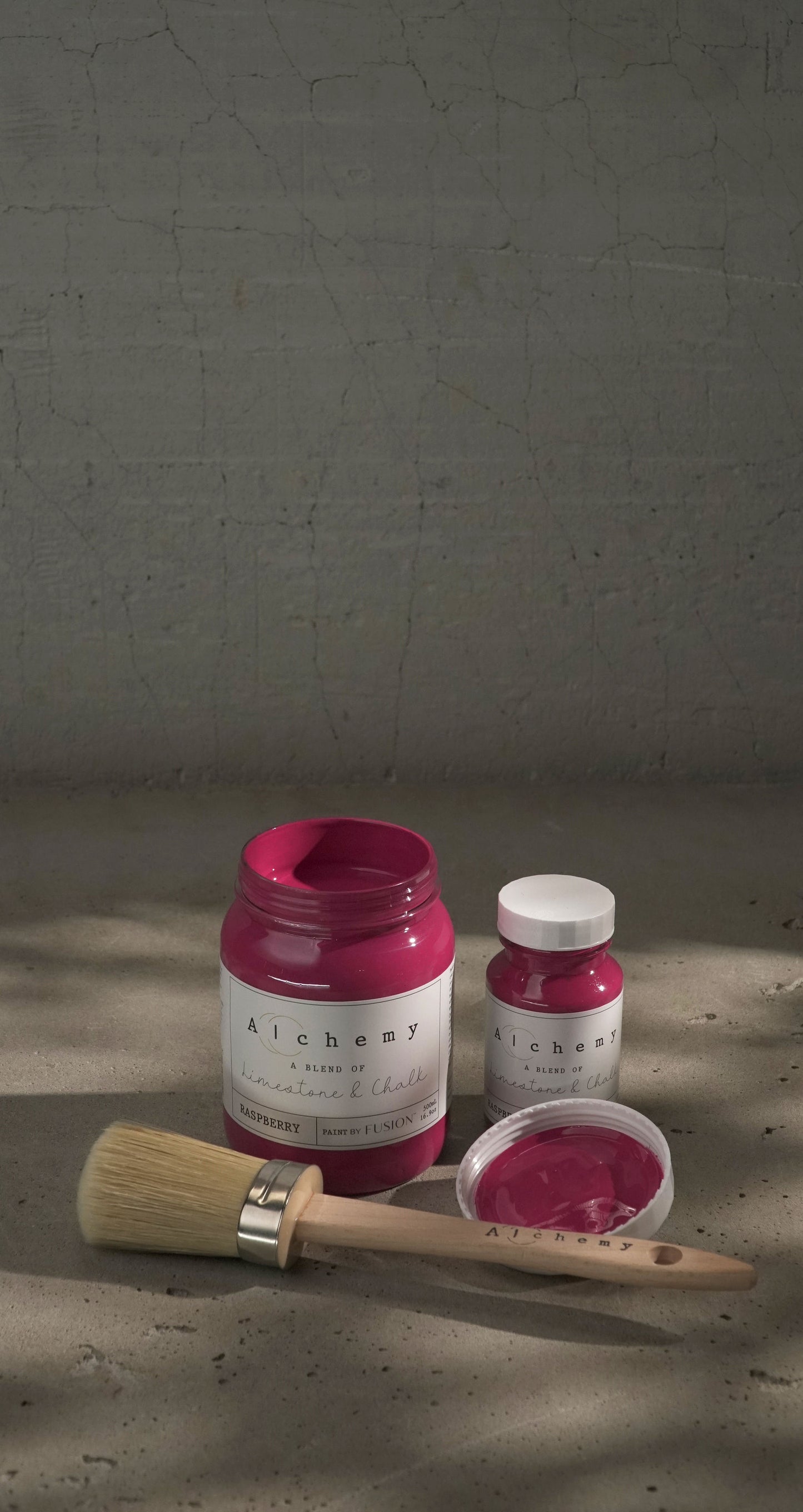 Two jars of pink paint with a brush on a textured surface