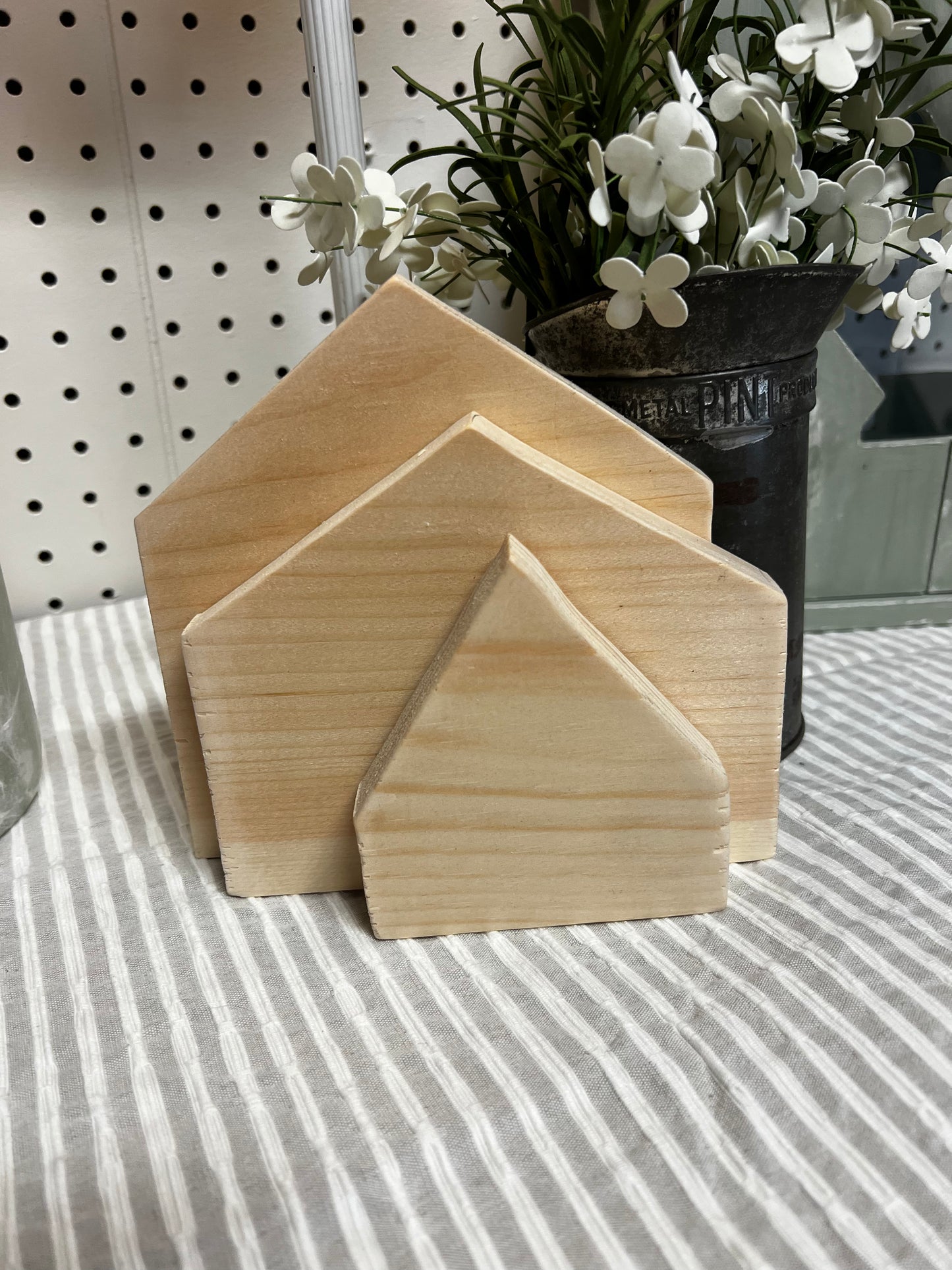 Three wooden house-shaped blocks on a striped surface with plants in the background.
