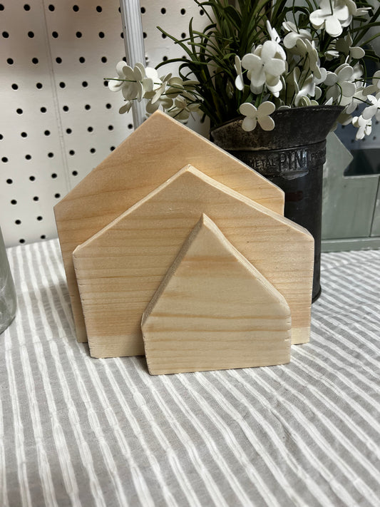 Three wooden house-shaped blocks on a striped surface with plants in the background.